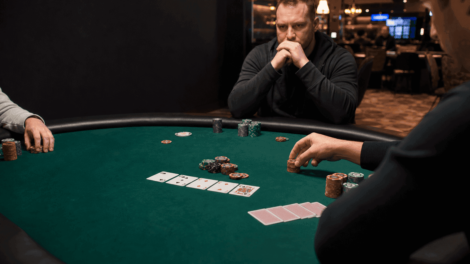 A man with clasped hands watches a small live Omaha pot from across the table.